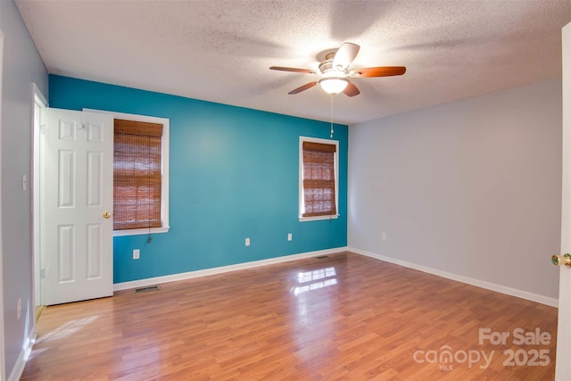 empty room with wood finished floors, a ceiling fan, visible vents, and a textured ceiling