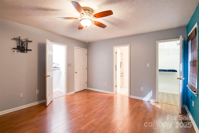 unfurnished bedroom with wood finished floors, baseboards, a spacious closet, a textured ceiling, and connected bathroom