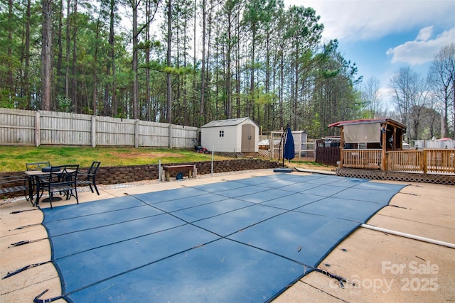 view of swimming pool featuring a deck, a fenced backyard, a storage shed, an outdoor structure, and outdoor dining area