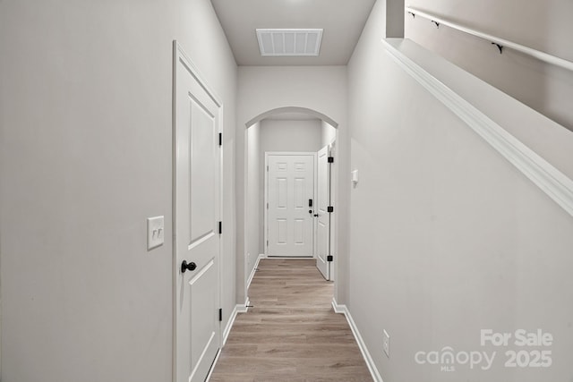 corridor with arched walkways, visible vents, light wood-style flooring, and baseboards