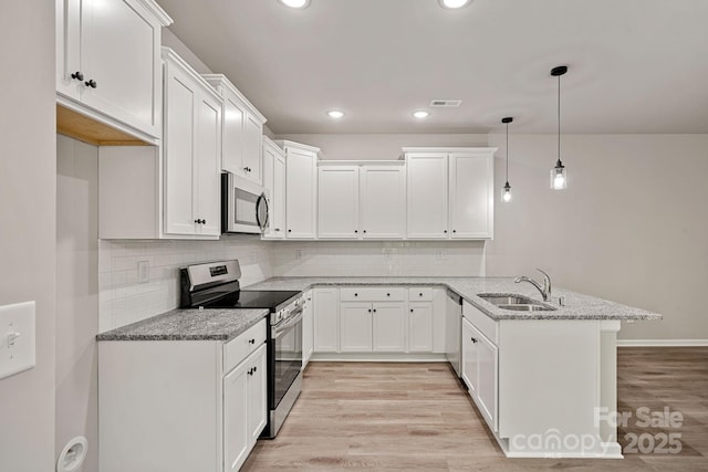 kitchen with a peninsula, a sink, stainless steel appliances, white cabinets, and light wood-style floors