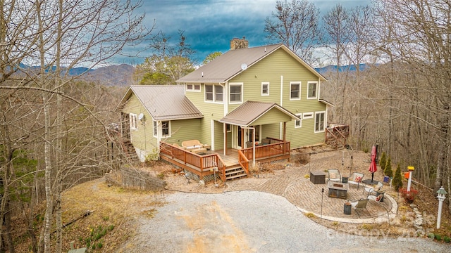 rear view of house featuring a fire pit, a deck with mountain view, a chimney, and a patio area