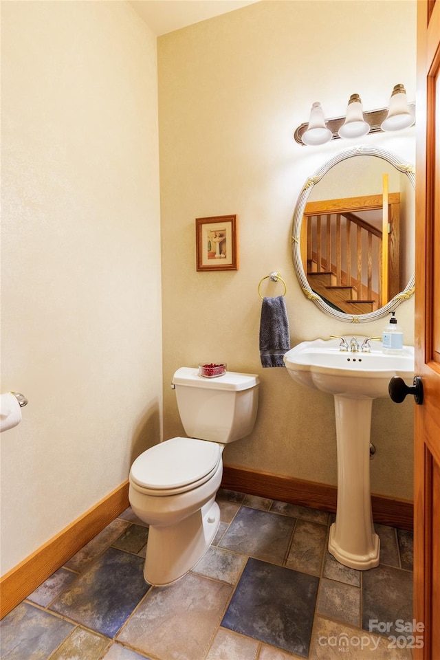 half bath with stone tile flooring, toilet, and baseboards