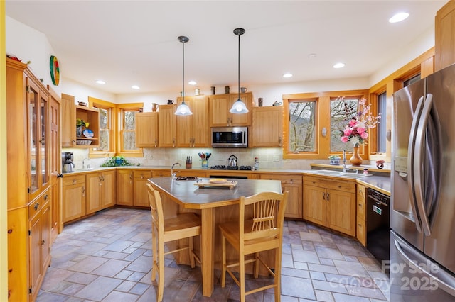 kitchen with an island with sink, decorative backsplash, stone finish floor, stainless steel appliances, and a sink