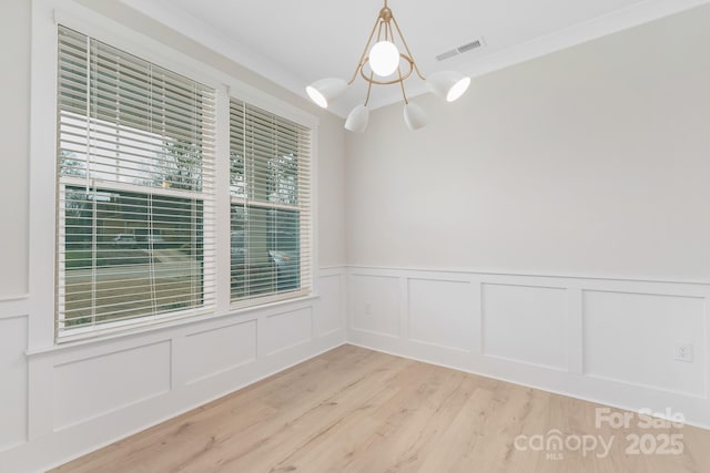 unfurnished room with visible vents, a notable chandelier, wood finished floors, and a decorative wall