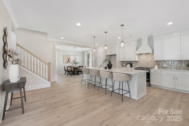 kitchen with stainless steel gas range oven, a breakfast bar, custom range hood, white cabinetry, and light wood-style floors