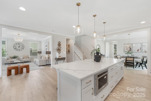 kitchen with white cabinetry, stainless steel microwave, light wood-style flooring, and a chandelier