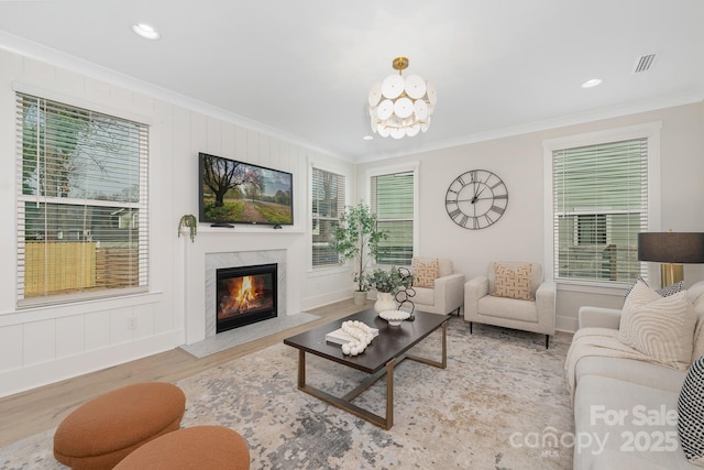 living room featuring visible vents, a notable chandelier, ornamental molding, wood finished floors, and a fireplace