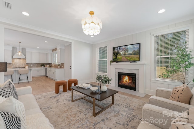 living room with crown molding, visible vents, a high end fireplace, and light wood-type flooring