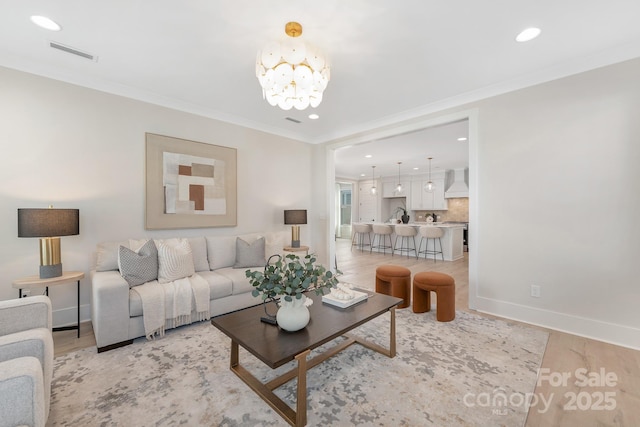 living room with visible vents, crown molding, baseboards, a chandelier, and light wood-style flooring