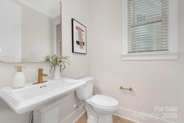 half bath with toilet, baseboards, and a sink