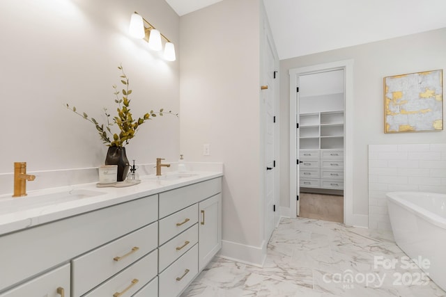 bathroom with a soaking tub, double vanity, marble finish floor, and a sink