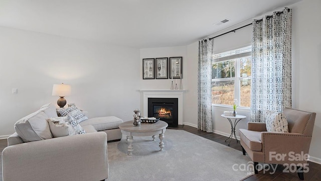 living room featuring visible vents, a fireplace with flush hearth, baseboards, and wood finished floors