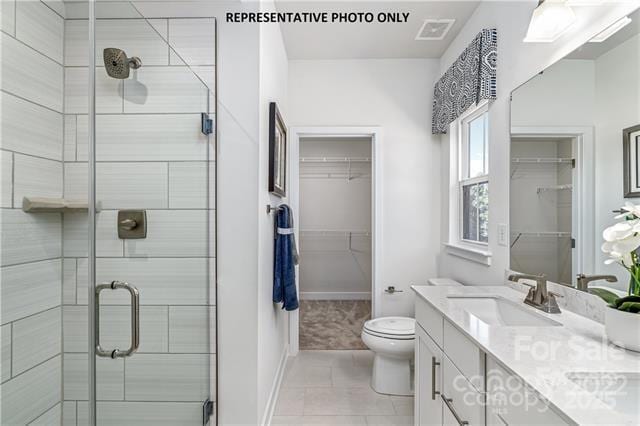 bathroom with a stall shower, toilet, a walk in closet, and a sink