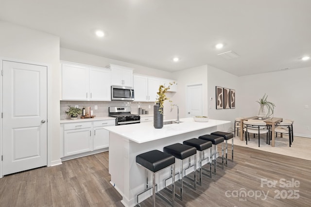 kitchen featuring a sink, a breakfast bar, appliances with stainless steel finishes, wood finished floors, and a kitchen island with sink