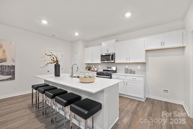 kitchen with a kitchen island with sink, a sink, decorative backsplash, white cabinets, and appliances with stainless steel finishes