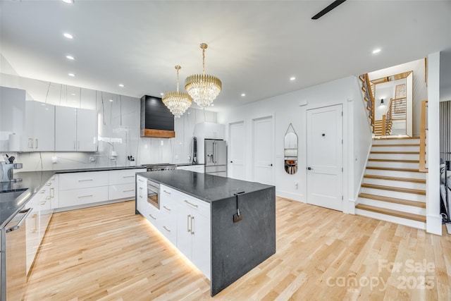 kitchen featuring a notable chandelier, light wood-type flooring, backsplash, dark countertops, and appliances with stainless steel finishes
