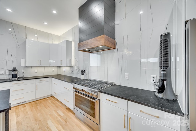 kitchen featuring backsplash, light wood-style floors, modern cabinets, wall chimney exhaust hood, and high end stove