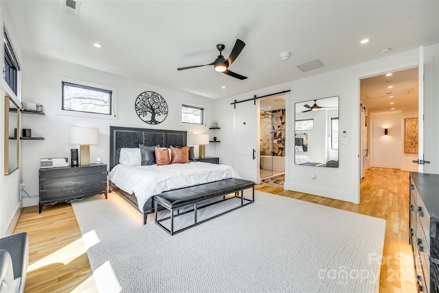 bedroom featuring light wood-style floors, visible vents, recessed lighting, a barn door, and baseboards
