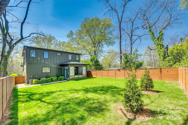 rear view of house featuring board and batten siding, a fenced backyard, central AC, and a lawn