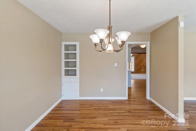 unfurnished dining area featuring a notable chandelier, wood finished floors, and baseboards