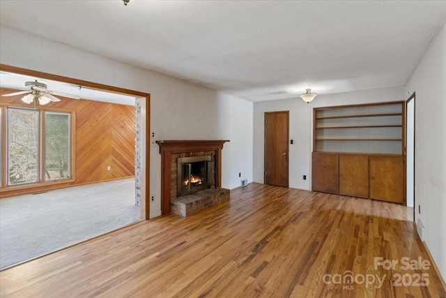 unfurnished living room with a ceiling fan, wood finished floors, a fireplace, and wood walls