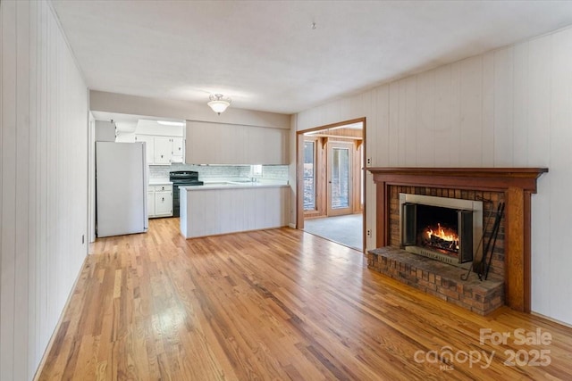 kitchen with a brick fireplace, light countertops, light wood-style flooring, freestanding refrigerator, and electric range