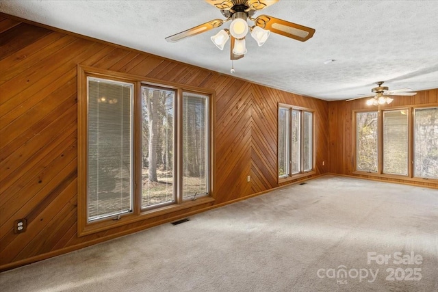 unfurnished room with visible vents, wooden walls, ceiling fan, and carpet flooring