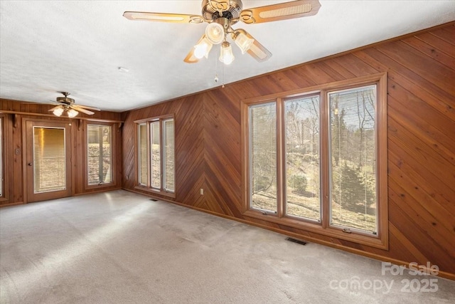 unfurnished room with wooden walls, carpet, a ceiling fan, visible vents, and a textured ceiling