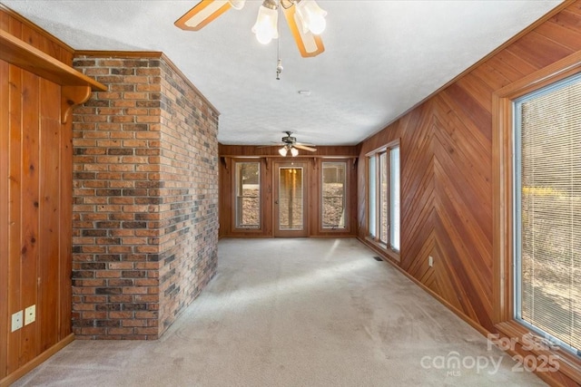 unfurnished living room featuring carpet floors, wooden walls, ceiling fan, and a textured ceiling