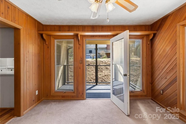 doorway to outside featuring a ceiling fan, french doors, wood walls, a textured ceiling, and light colored carpet