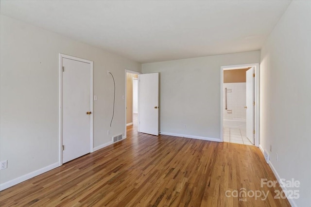 unfurnished bedroom featuring visible vents, ensuite bathroom, baseboards, and wood finished floors