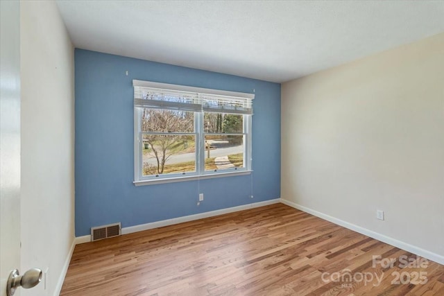 spare room featuring wood finished floors, visible vents, and baseboards