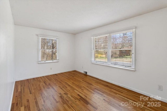 unfurnished room featuring wood finished floors, visible vents, a wealth of natural light, and baseboards