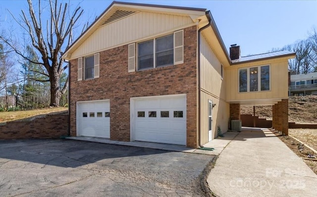view of home's exterior featuring cooling unit, driveway, a chimney, a garage, and brick siding