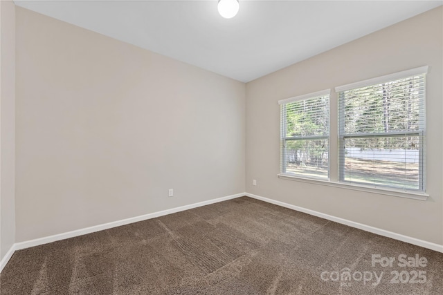unfurnished room featuring baseboards and dark colored carpet