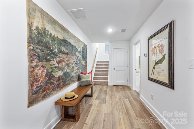 hallway with stairway, baseboards, visible vents, and light wood finished floors