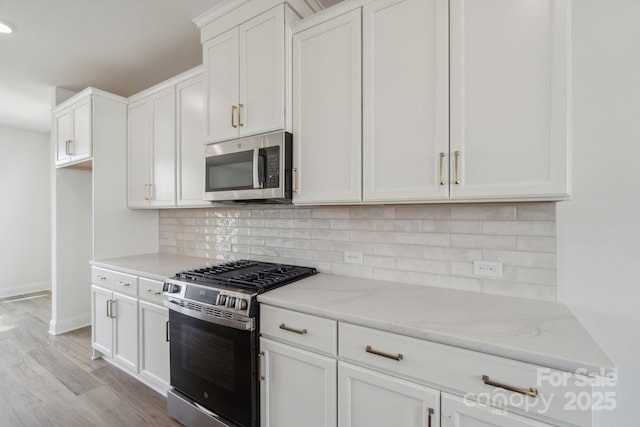 kitchen with light stone counters, stainless steel appliances, backsplash, and white cabinets