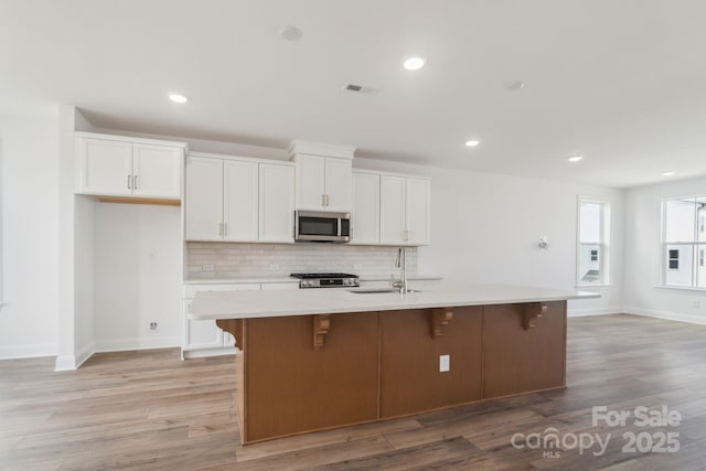 kitchen featuring visible vents, a sink, stainless steel microwave, range, and backsplash