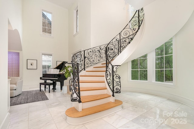 1665 Sterling Rd, Charlotte, NC 28209 - staircase featuring marble finish floors, a towering ceiling, plenty of natural light, baseboards, and arched walkways