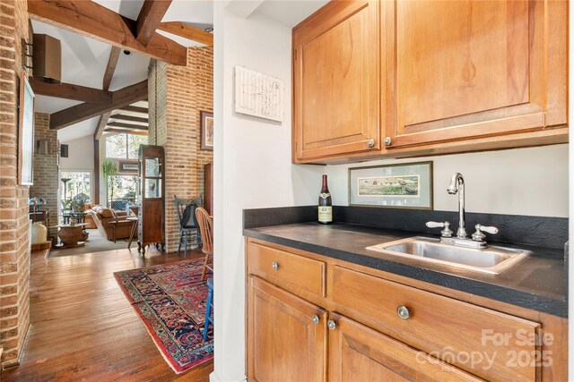 32 Fairway Rdg, Lake Wylie, SC 29710 - kitchen featuring wood finished floors, brick wall, lofted ceiling with beams, a sink, and dark countertops