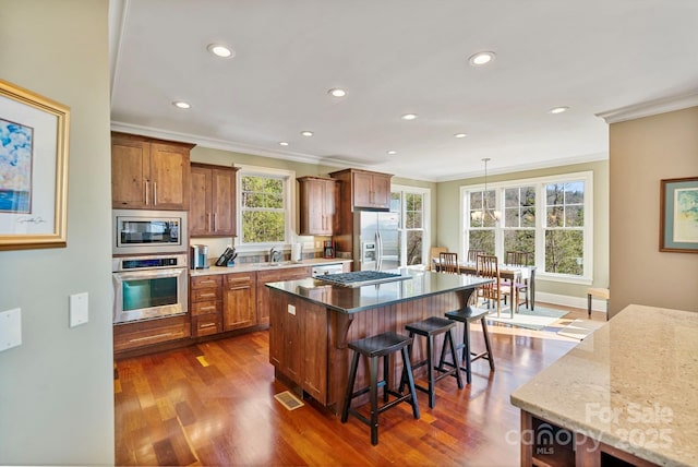 kitchen with brown cabinetry, dark wood-style flooring, stainless steel appliances, a kitchen breakfast bar, and a center island