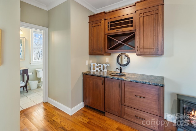 bar featuring ornamental molding, baseboards, light wood finished floors, and a sink