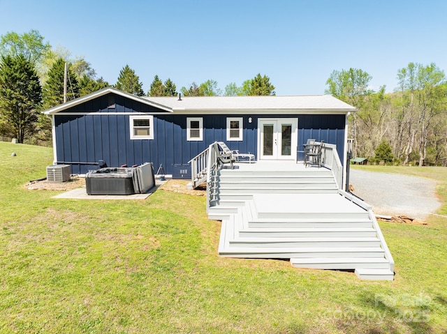 rear view of house with board and batten siding, a wooden deck, a lawn, french doors, and central AC unit