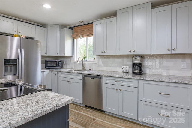 kitchen featuring backsplash, light stone countertops, appliances with stainless steel finishes, pendant lighting, and a sink