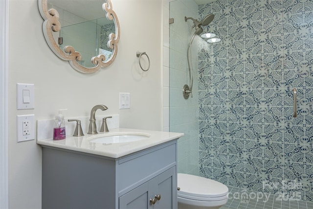 full bath with vanity, a tile shower, and toilet
