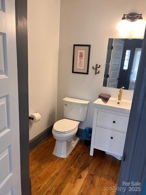 half bathroom with toilet, vanity, baseboards, and wood finished floors