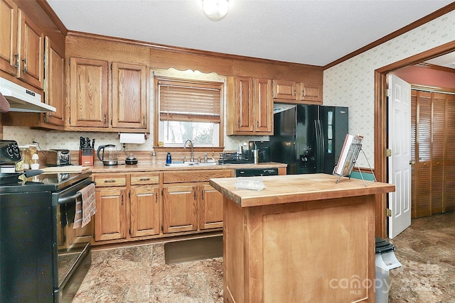 kitchen with wallpapered walls, a sink, black appliances, under cabinet range hood, and butcher block counters