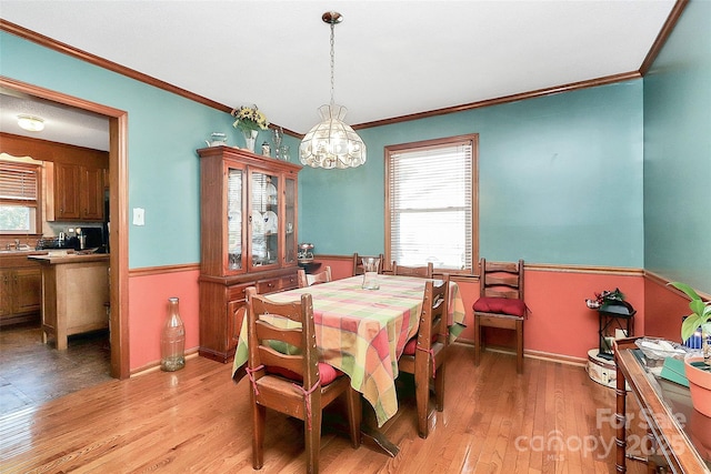 dining space with ornamental molding, an inviting chandelier, wainscoting, light wood finished floors, and baseboards