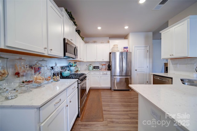 kitchen with white cabinetry, light stone counters, tasteful backsplash, and appliances with stainless steel finishes